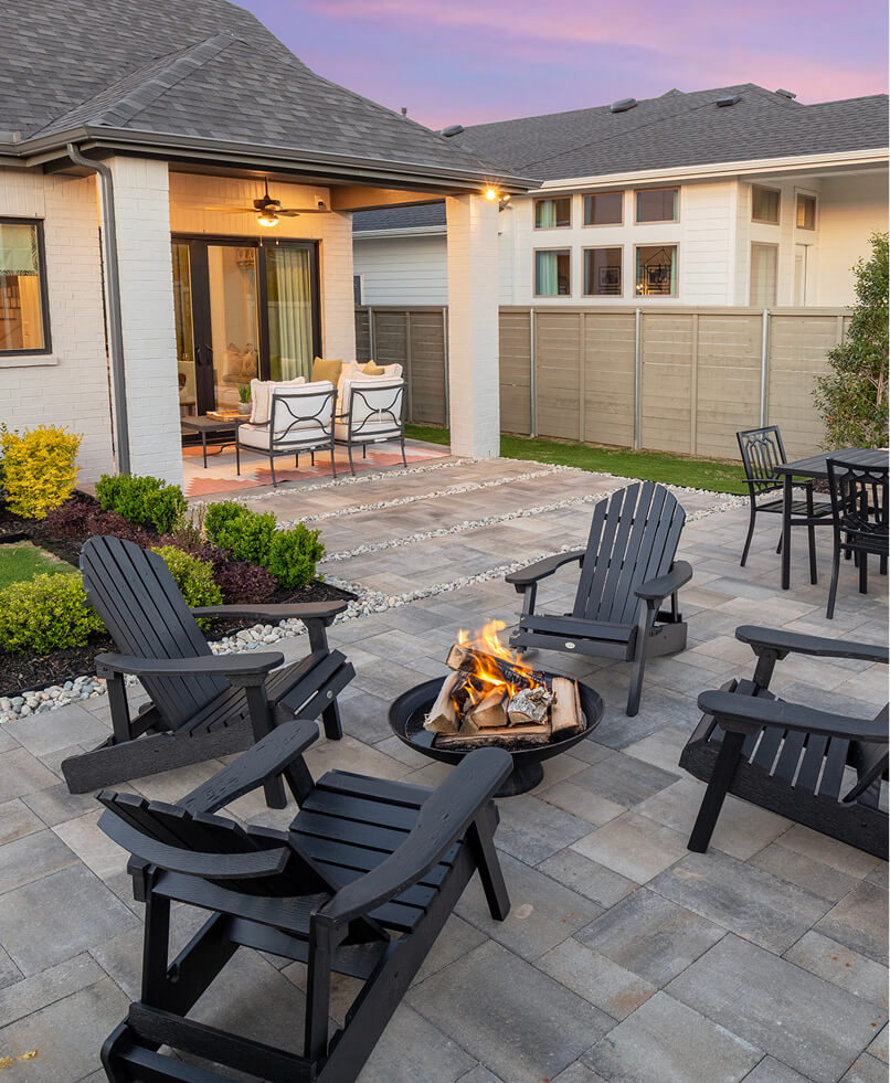A modern backyard patio in one of the stunning new homes Celina TX offers, featuring Adirondack chairs around a fire pit, outdoor dining set, and a covered seating area near the house at sunset.