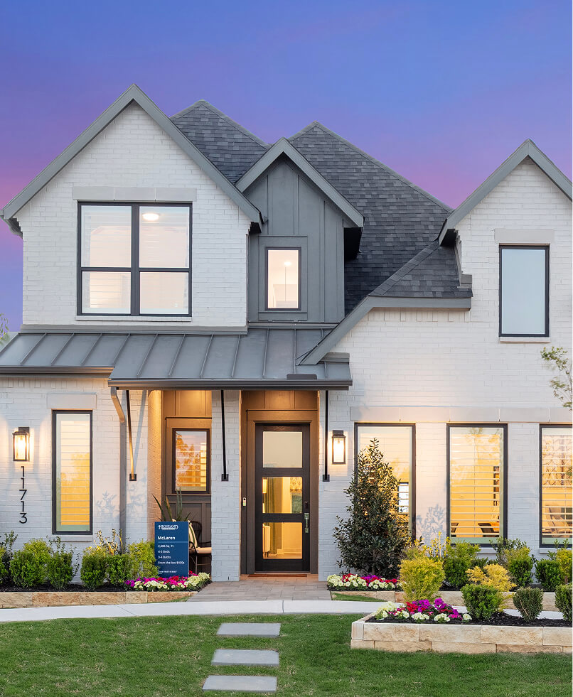 Two-story modern house with white brick exterior, large windows, and a manicured front lawn with flowers, photographed at dusk—an ideal example of new homes in Celina TX.