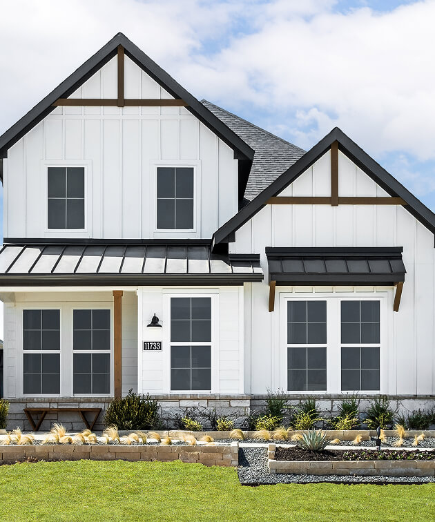 A modern two-story house with white siding, black trim, and a metal roof awning, this property is an ideal example of new homes Celina TX buyers love, featuring a landscaped front yard with rocks and plants.