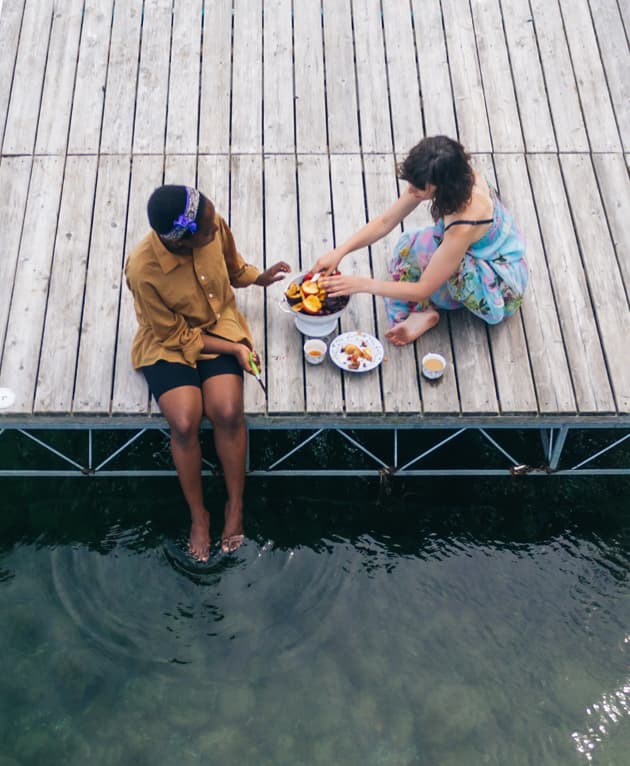 A rendering shows a wooden dock extending over water with several people on it, connected to a landscaped park area with trees, paths, and benches—perfect for residents of Ramble homes in the vibrant New homes Celina TX community.