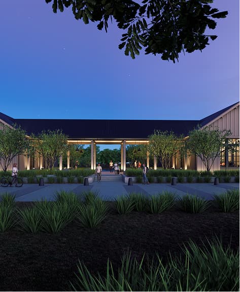 Modern building with a covered walkway, surrounded by trees and landscaped greenery, illuminated at dusk with people walking nearby.